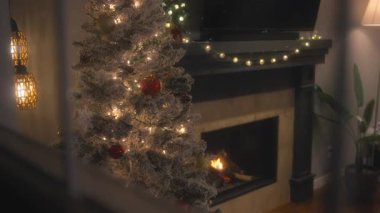Dışarıda kar yağarken, evde bir Noel ağacının yanında şömine yanıyor. Dolly çekim, yavaş çekim, pencere görünümü. 