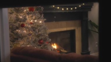 Dışarıda kar yağarken, evde bir Noel ağacının yanında şömine yanıyor. Yavaş çekim. 