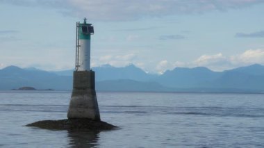 Okyanus körfezi sularında arka planda karlı dağlar olan bir deniz feneri kulesi. Yavaş çekim.