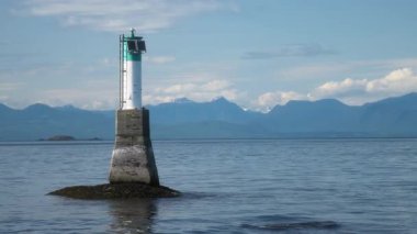 Okyanus körfezi sularında arka planda karlı dağlar olan bir deniz feneri kulesi. Yavaş çekim.