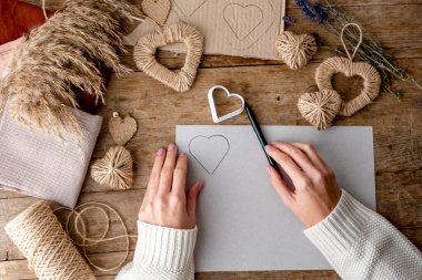 Sıfır Sevgililer Günü konseptini boşa harcamak ve taklit etmek. Kadın elleri şablon kalp çizer. Furoshiki paketi için tekstil, el işi kağıtları, lavanta ve jüt kalplerle dekorasyon. Üst görünüm veya düz uzanma.