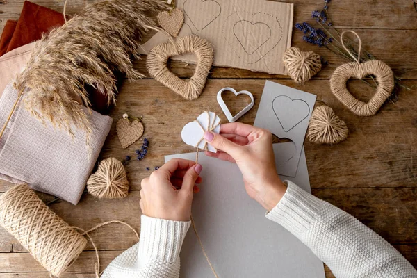 Zero waste Valentine\'s Day concept and mock up. Female hands to cut stencil heart. textile for the furoshiki package, craft paper for do it youself decor with lavender and jute hearts. Top view or flat lay.