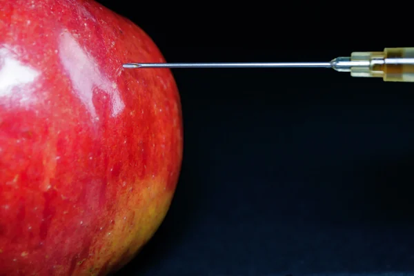 Aguja hipodérmica inyectando una manzana roja — Foto de Stock