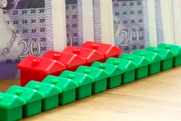 Modelos de casa de plástico rojo verde en una fila diagonal con billetes de banco — Foto de Stock