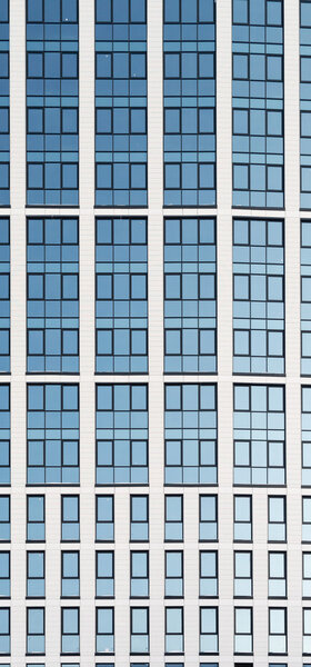 Modern glass high-rise office building with acute angles showing reflections of a bright blue clear sky. Nobody in the image and copy space area for business finance or architectural designs.