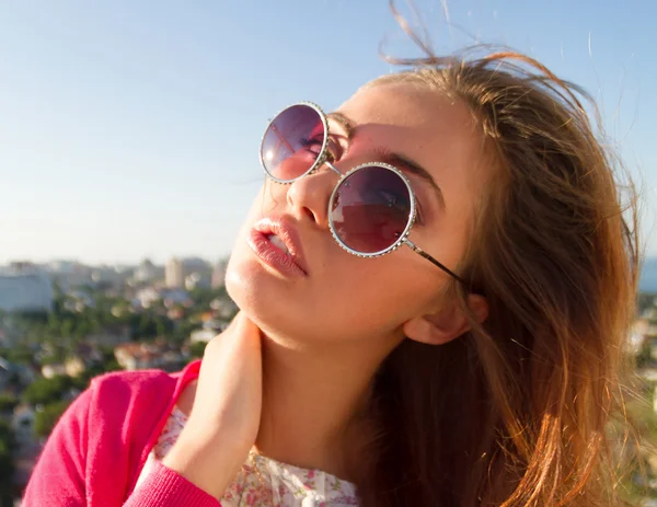 Summer close up fashion portrait of attractive astonish girl posing on background of the amazing view of city from the roof. in the pink outfit and round pink sunglasses. The amazing view terrace — Stock Photo, Image