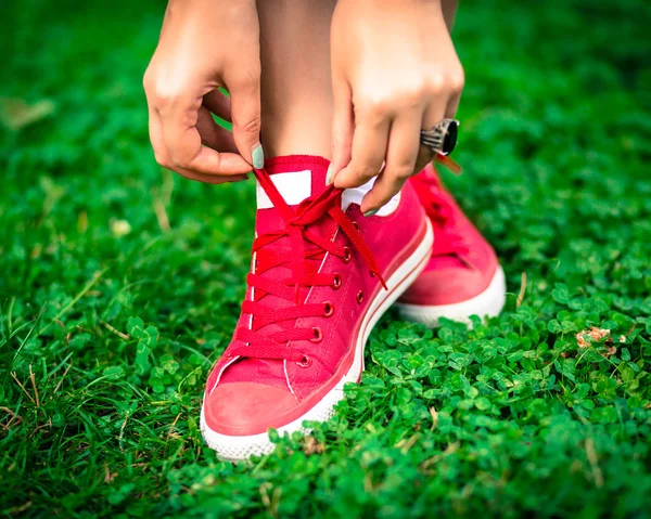 De cerca la foto de moda de las zapatillas de deporte femeninas de color rosa brillante y las manos atando cordones de zapatos. Imagen de moda de piernas de mujer, con elegantes camas y anillo de diamante grande, permaneciendo en la hierba, colores brillantes . —  Fotos de Stock