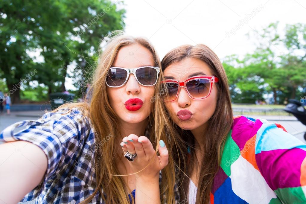 Close up lifestyle selfie portrait of pretty fresh young brunette and blonde best friends girls making selfie,having fun,sending kisses,wearing sunglasses. Fresh make-up,teenage outfit,summer vacation