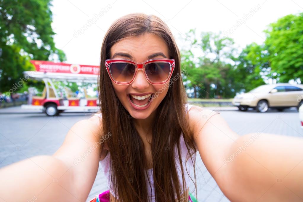 Stylish lady in casual shirt and jeans strikes selfie pose, holds  smartphone, gently touches face, isolated on blue background. 25863421  Stock Photo at Vecteezy