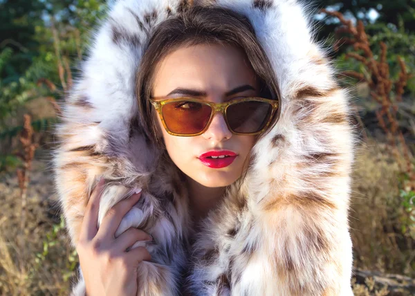 Moda de cerca Retrato de mujer atractiva y elegante con labios rojos con abrigo de piel y gafas de sol retro de moda — Foto de Stock