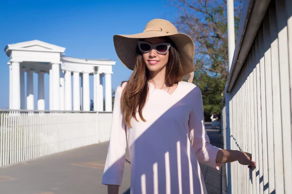 Şehirde yürüyüş güzel ve genç birbayan. Fashion.Wearing şirin pembe elbise, geniş şapka, kedi gözlük. Güneşli havalarda günde beyaz elbise ve hasır şapka giyen oldukça neşeli kadın portresi. — Stok fotoğraf