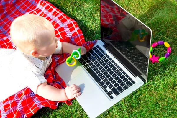 Bambino carino che gioca con il computer portatile e giocattoli all'aperto su erba verde. bambino stupito guarda lo schermo del notebook — Foto Stock