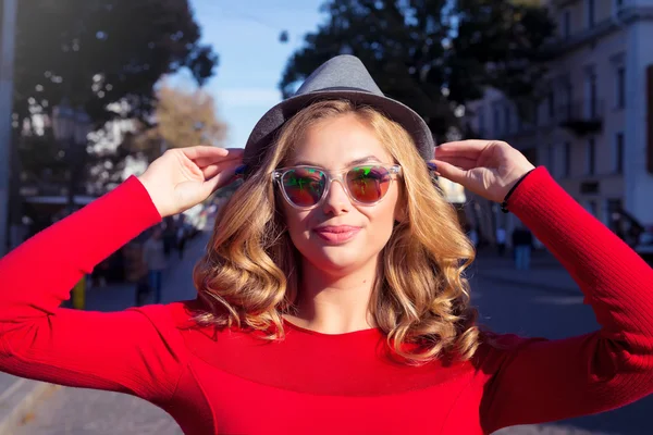 Hermosa joven caminando por la ciudad. Fashion.Portrait de la hermosa chica de moda al aire libre en el soleado día de primavera, con vestido casual rojo, gafas de sol de moda y sombrero retro gris. Feliz, positivo — Foto de Stock