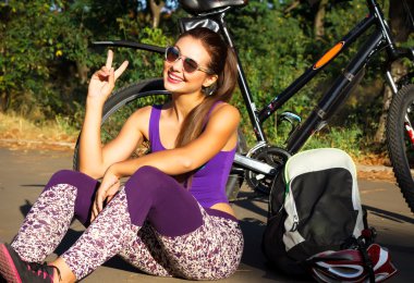 Colorful outdoor portrait of young pretty fashion model with bike. Young brunette sexy woman posing in summer. beautiful young woman sitting next to her bike outdoors wearing trendy sportswear
