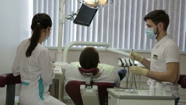 Joven dentista y su asistente tratar dientes de mediana edad hombre — Vídeos de Stock