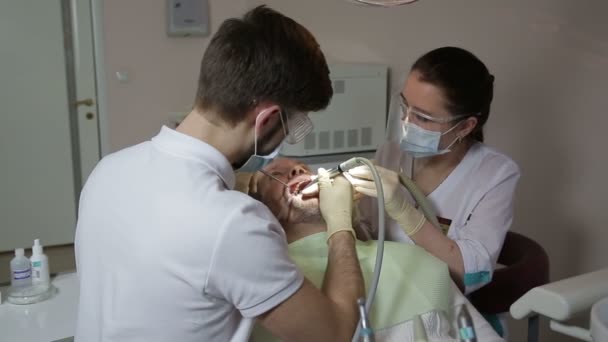 Young dentist and his assistant treat teeth middle-aged man — Stock Video