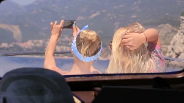 Two girls taking pictures on the phone sitting on the bow of the boat — Stock Video