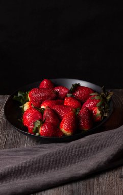 Siyah arkaplanlı çilek tabağının dikey görünümü.