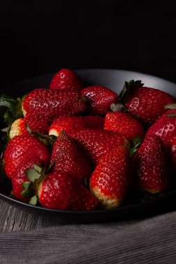 Siyah arka planı olan siyah bir tabakta çilekler..