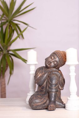 Beyaz arka planda beyaz bir masada iki beyaz mum ve bir bitki..