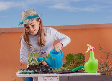 Çiftlik arazisi ve sulama tenekesi olan bir masada bahçeyle ilgilenen bir kız..