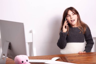 Cep telefonuyla konuşan ve sol tarafında bilgisayarı olan bir kız.