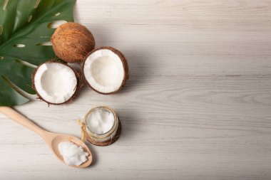 Hala iki hindistan cevizinin hayatı var, biri ikiye bölünmüş, bir kavanoz hindistan cevizi yağı ve sağda yazı için yeri olan tahta bir kaşık.