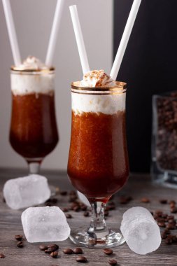 İki bardak buzlu kahve manzarası, biri ön planda buz küpleri ve bardakların etrafında kahve çekirdekleri.