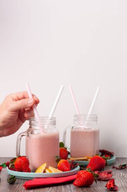Çilekli ve bisküvili smoothie konsepti. Bir eliyle meyve suyu içmek için kamışa uzanıyor.