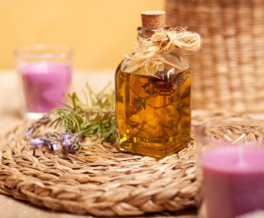 Bir kavanoz lavanta yağı, iki lavanta kokulu mum ve sarı arkaplanda bir demet lavanta çiçeği..