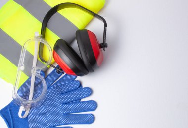 Güvenlik gözlükleri, yansıtıcı yelek, iş eldivenleri ve beyaz arka planda işitme koruyucu kasklar gibi çeşitli öğelerin kavramları
