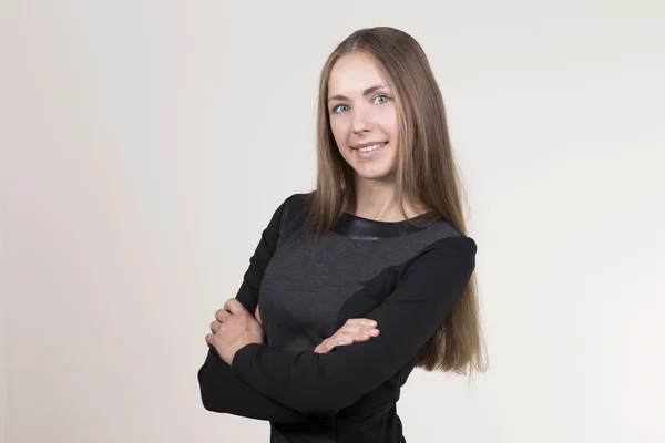 Jolie jeune femme souriante dans une robe noire regardant la caméra. mains croisées — Photo