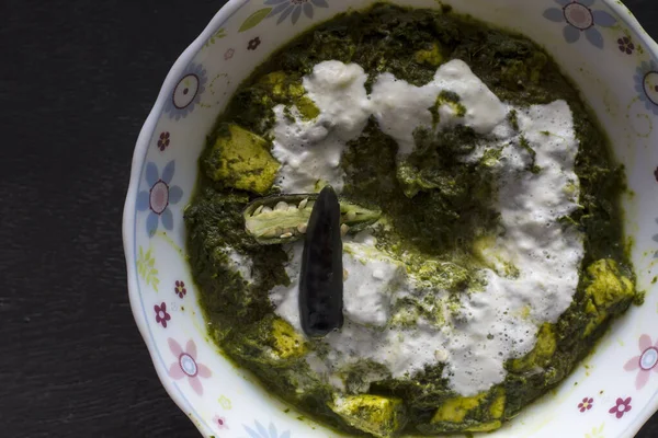 Popüler Palak paneer veya ıspanak ve koyu arkaplanda süzme peynir körisi. Seçici odaklı taze kremayla süslenmiş geleneksel Hint yemeği..