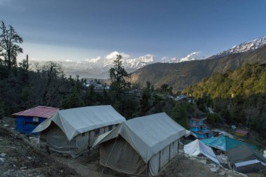 Dağ yolu mavi gökyüzü ve kar kaplı iki lüks çadır ile kıvrılır.
