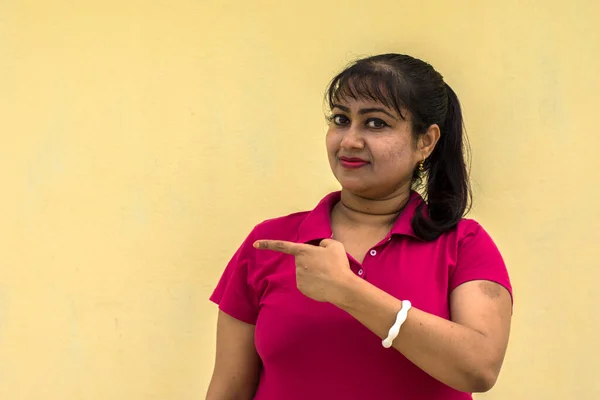 Hintli kadın model mutlu görünüyor, hafifçe gülümsüyor, işaret parmağıyla işaret ediyor, gülümsüyor, gülümsüyor, sarı arka planda elinde bir kalem var, metin için. Mutlu ruh hali konsepti.