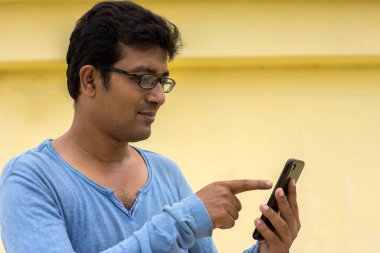 Genç ve yakışıklı Hintli erkek cep telefonunu izliyor.