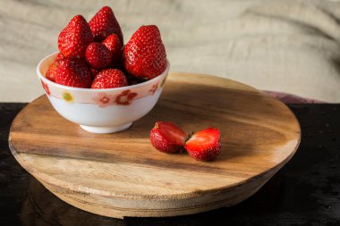 İki parçaya ayrılmış taze organik kırmızı çilek ve biraz da ahşap masadaki kasede. Seçici odak.