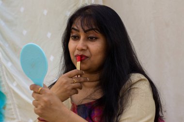 Güzel bir Hintli kadın ruj sürüp eline ayna tutarken hazırlanıyor. Metni kopyalamak için beyaz arkaplan.