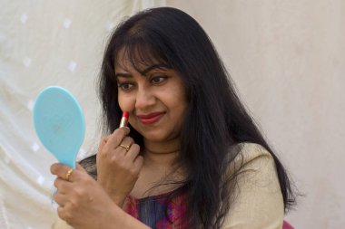 Güzel bir Hintli kadın ruj sürüp eline ayna tutarken hazırlanıyor. Metni kopyalamak için beyaz arkaplan.