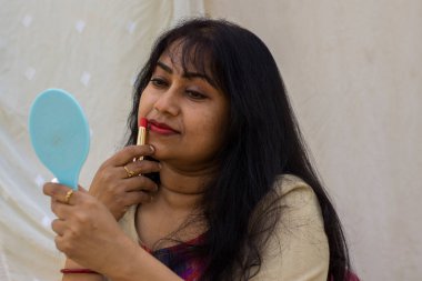 Güzel bir Hintli kadın ruj sürüp eline ayna tutarken hazırlanıyor. Metni kopyalamak için beyaz arkaplan.