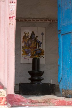 Batı Bengal, Baraipur yakınlarındaki Shiva tapınağında arkasında Lord Shiva fotoğrafı olan siyah bir Şiva putu..