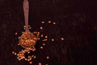 Bir çay kaşığı dolusu metit ya da çemen otu, üzerinde az miktarda çiğ kimyon tohumu olan siyah ahşap bir masa. Seçici odak.