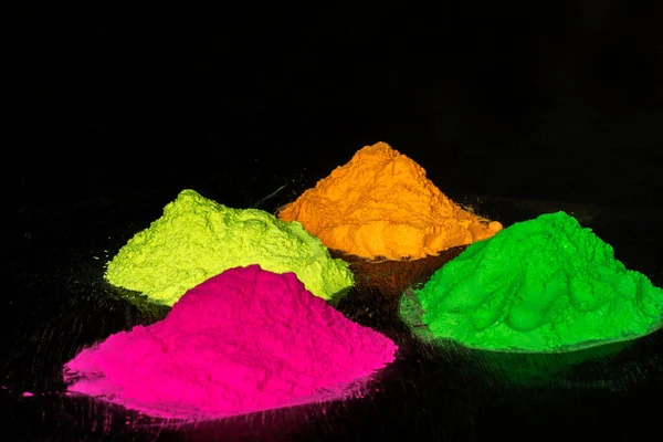 Siyah ahşap arka planda organik turuncu, yeşil, pembe ve sarı bitkisel gülal veya Holi renkleri. Seçici odak.