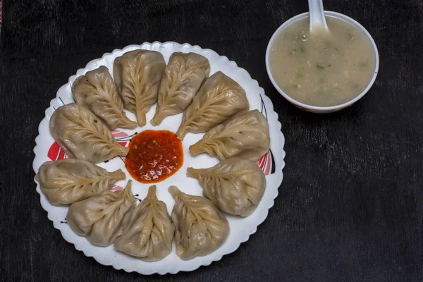 Bir tabak dolusu Momo soslu tavuk ve siyah arka planda çorba. Seçici odak.