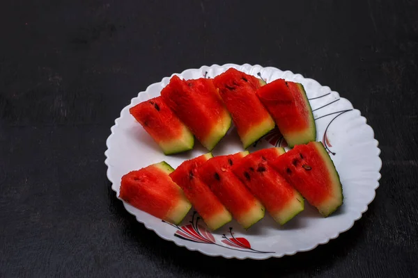 Siyah ahşap bir yüzey üzerinde beyaz bir tabakta kırmızı taze kesilmiş karpuz meyvesi. Seçici odak.