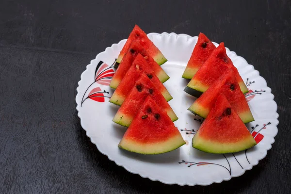 Siyah ahşap bir yüzey üzerinde beyaz bir tabakta kırmızı taze kesilmiş karpuz meyvesi. Seçici odak.