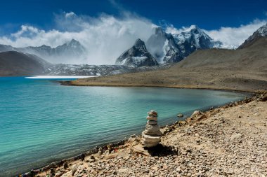 Gurudongmar Gölü 'nün çok güzel bir manzarası. Üzerinde kayalar ve arka planda mavi gökyüzü olan bir dağ var. Gurudongmar Gölü, Hindistan ve dünyanın en yüksek göllerinden biridir. Hindistan 'ın Sikkim eyaletinde 17.800 feet yükseklikte yer almaktadır..