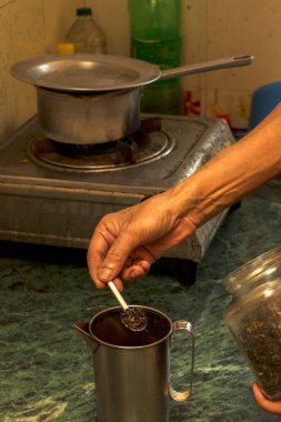 Çelik çay demliğine çay yaprağı koyarak çay yapmakla meşgul yaşlı bir adam. Seçici odak.