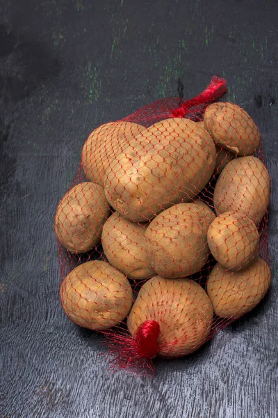 Een Netzak Vol Aardappelen Een Zwarte Achtergrond Met Selectieve Focus — Stockfoto