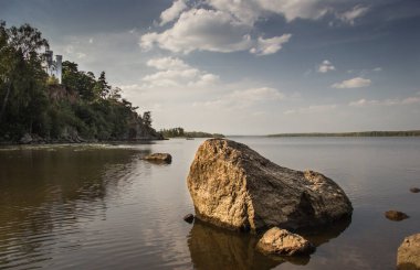 Göl, suda büyük bir kaya, bulutlu bir gökyüzü. Monrepos Parkı. Vyborg